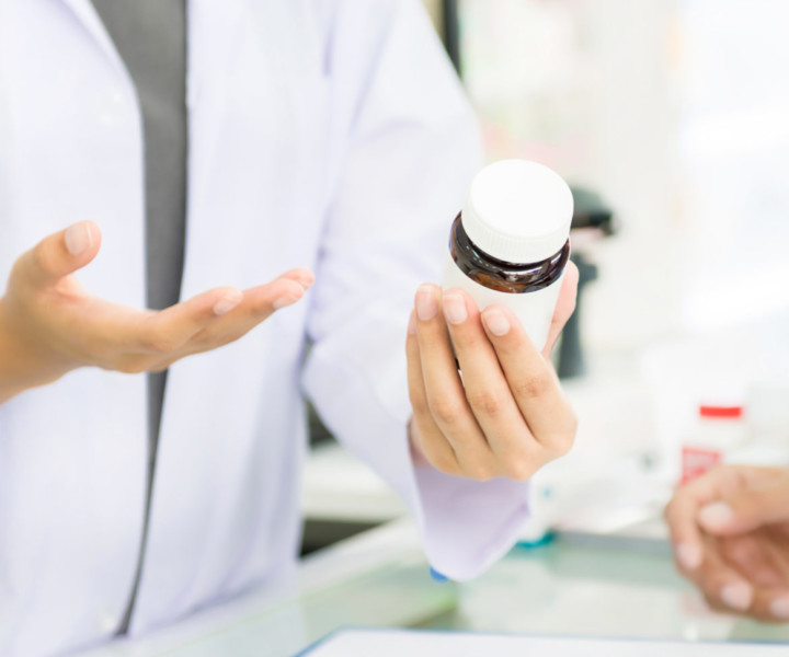 Female pharmacist holding medicine bottle giving advice to customer in chemist shop or pharmacy - horizontal web banner with copy space on the left