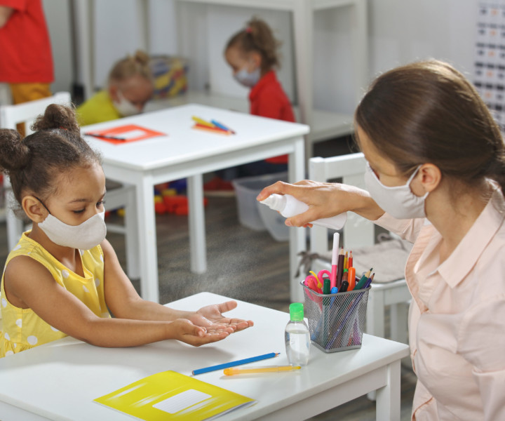 A teacher helps a student with hand sanitizing in the classroom