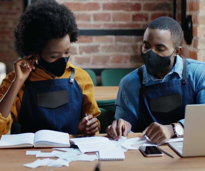African American couple in masks doing business calculations of restaurant and checking bills. Calculating spends and damages. Reopen after lockdown. Counting at laptop computer Small entrepreneurship