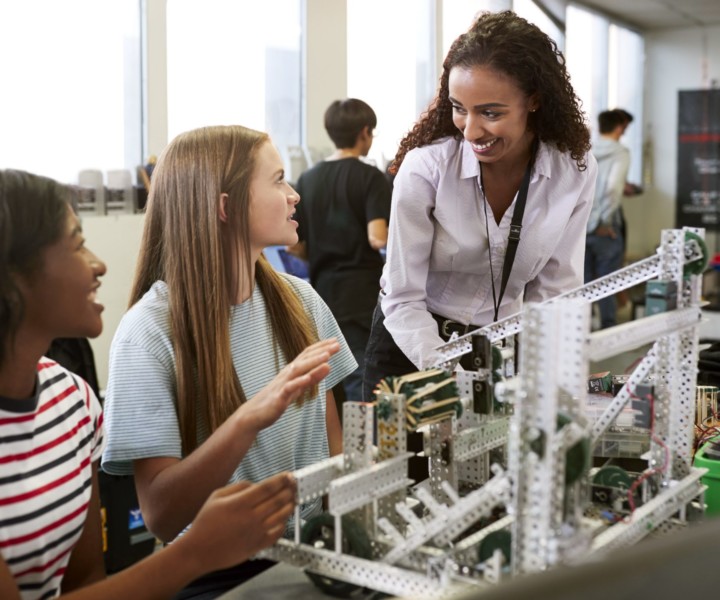 Woman Teacher With Female College Students Building Machine In Science Robotics Or Engineering Class