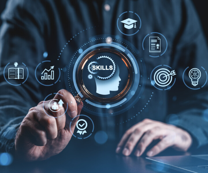Person holding magnifying glass over digital icons symbolizing skills and learning, modern graphic style, dark blurred background, concept of professional development and education