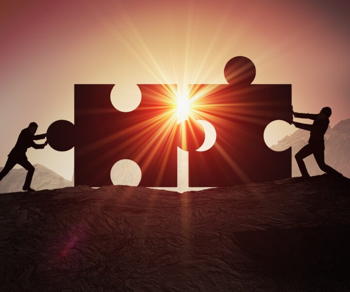 Teamwork, partnership and cooperation concept. Silhouettes of two businessman joining two pieces of puzzle together.